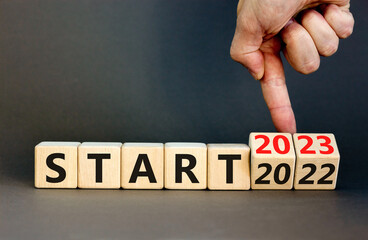 2023 start new year symbol. Businessman turns a wooden cube and changes words Start 2022 to Start 2023. Beautiful grey table grey background, copy space. Business 2023 start new year concept.