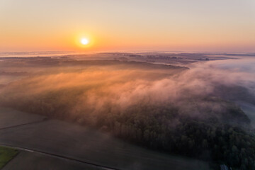 Bright orange rising sun over forest and farm field covered in thick morning fog. Roztocze Poland. Horizontal shot. High quality photo