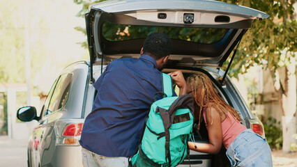 African american couple loading voyage luggage and trolleys inside car trunk while getting ready for holiday citybreak departure. People putting baggage inside vehicle while going on field trip.
