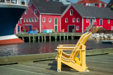 Yellow Adirondack chairs on Lunenburg pier. Colourful building and boats are visible in background