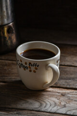 A cup of black coffee and a geyser on a wooden table.