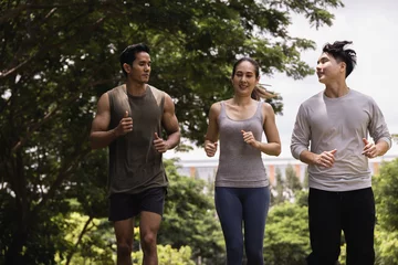 Fotobehang Asian young man and woman jogging together in green park. Concept for healthy lifestyle and oudoor life. © Panithan