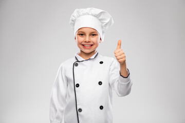 cooking, culinary and profession concept - happy smiling little boy in chef's toque and jacket showing thumbs up over grey background