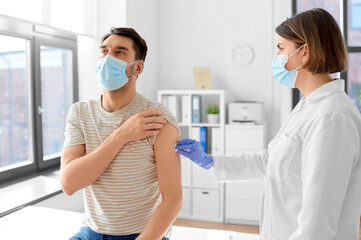 health, medicine and pandemic concept - female doctor or nurse in protective medical mask and gloves disinfecting male patient's skin at hospital