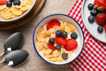 Delicious crispy cornflakes with milk and fresh berries on wooden table, flat lay