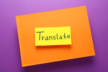 Card with word Translate and sheet of orange paper on violet background, top view