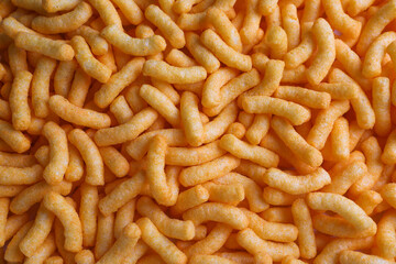Many crunchy cheesy corn puffs as background, top view