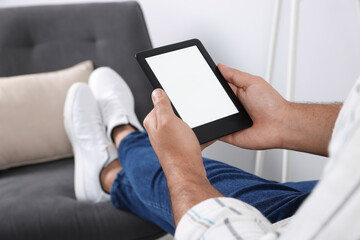 Man using e-book reader indoors, closeup view
