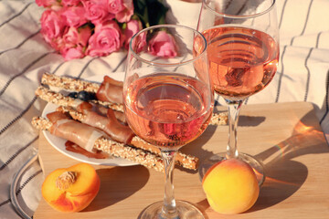Glasses of delicious rose wine, flowers and food on white picnic blanket, closeup