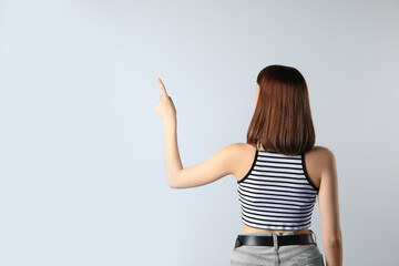 Young girl pointing on white background, back view. Space for text