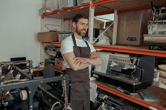 Male barista in uniform on warehouse with coffee machines and other professional equipment
