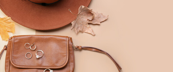 Hat, handbag, jewelry and autumn leaves on beige background with space for text