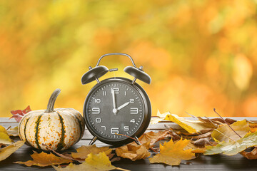 Alarm clock with autumn leaves and pumpkin on wooden table outdoors