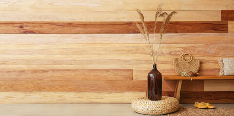 Vase with floral decor, pouf, bench and female accessories near wooden wall