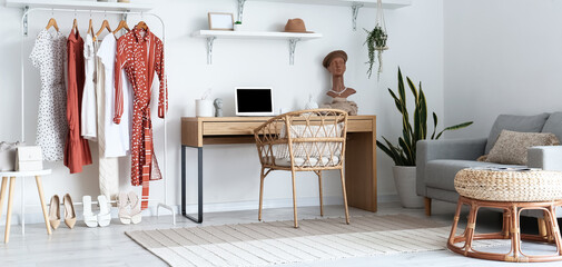 Interior of light room with workplace and rack with female clothes