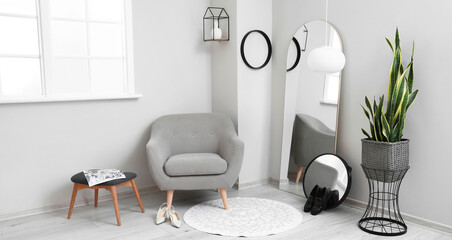 Interior of light room with mirrors, grey armchair and houseplant