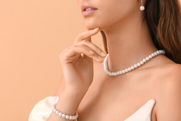 Beautiful young woman with stylish pearl jewelry on beige background, closeup
