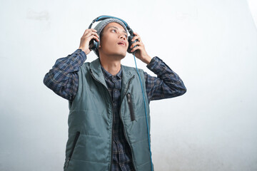 asian young man wearing dark blue vest and beanie wearing headphones, isolated on white background focused on listening to music via smartphone