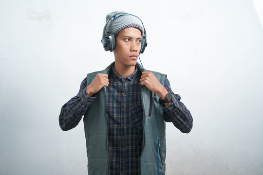 Asian Young Man Wearing Dark Blue Vest And Beanie Wearing Headphones, Isolated On White Background Quirky And Trendy While Listening To Music