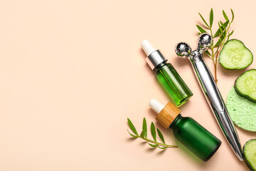 Facial massage tool with cosmetic dropper bottles, cucumber slices and plant branches on beige background