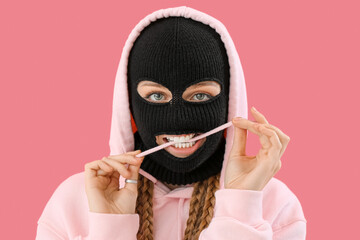 Young woman in balaclava biting lace on pink background