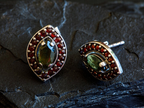 Women's earrings in eye shape with Czech red garnet and green moldavit or vltavin gemstone on black natural background
