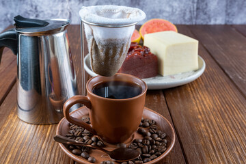 Cup of coffee surrounded by beans, cloth filter and guava sweet and curd cheese.