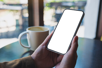 Mockup image of hands holding mobile phone with blank desktop screen with coffee cup on the table