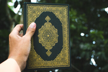 green holy-quran in hand on green nature background, koran is holy book of muslim religion to prayer for god allah, with copy space for text written