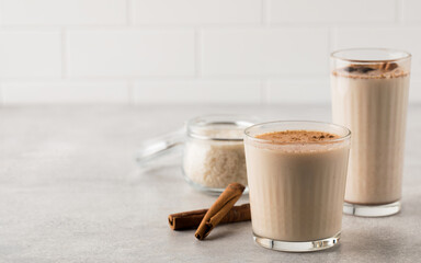 Glasses with a cold drink based on Horchata rice, cinnamon sticks and a jar of rice on a light background. Copy space