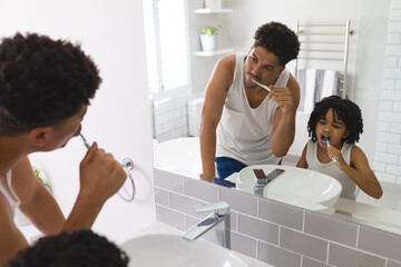 Mirror reflection of hispanic father and son brushing teeth together in bathroom - Powered by Adobe