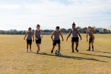 Multiracial elementary schoolboys playing soccer on school soccer field against sky