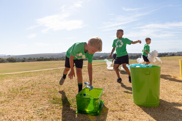Multiracial elementary schoolboys putting plastic garbage in garbage bin on school ground