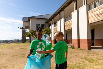Multiracial elementary schoolboys collecting plastic in garbage bag during sunny day