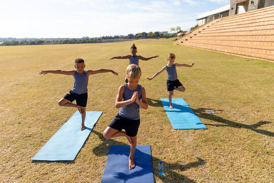 Multiracial elementary schoolboys with arms outstretched and hand clasped standing on one leg on mat