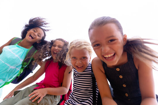 Low angle portrait of cheerful multiracial elementary schoolgirls standing against sky