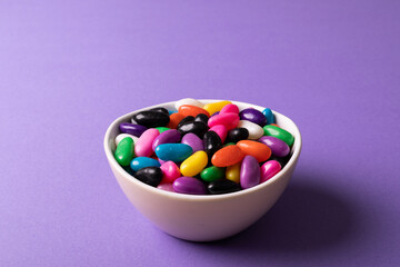 Close-up of multi colored candies in white bowl on purple background with copy space
