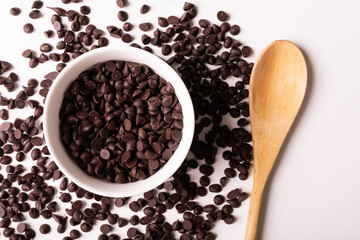 Overhead view of fresh chocolate chips with bowl and wooden spoon on white background - Powered by Adobe