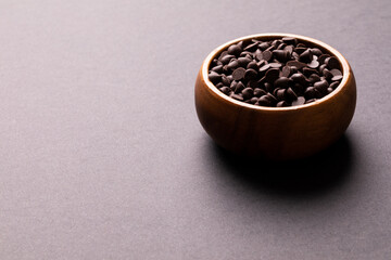 High angle view of fresh chocolate chips in wooden bowl against colored background with copy space
