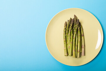 Directly above view of green raw asparagus in white plate by copy space against blue background