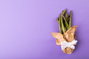 Overhead view of copy space by asparagus bunch tied in paper with ribbon on purple background - Powered by Adobe