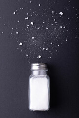 Overhead view of salt shaker and fallen salt on black table