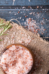 Close-up of himalayan pink rock salt in wooden bowl with rosemary on jute fabric over table