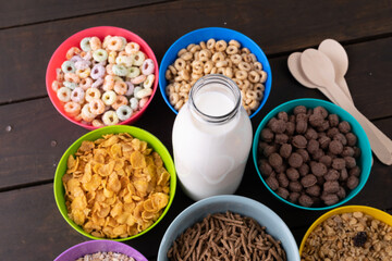 High angle view of various breakfast cereals in bowls arranged with milk bottle on table