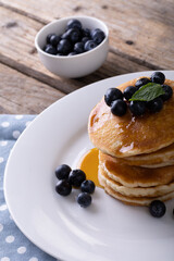 Close-up of appetizing pancakes with syrup, herb and blueberries served in plate on table