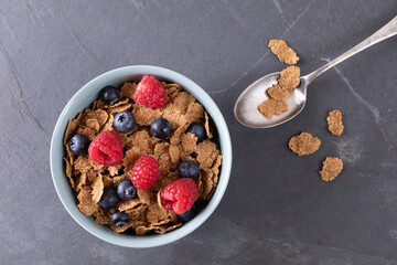 Directly above shot of blueberries and raspberries with cornflakes in bowl by spoon on food slate - Powered by Adobe