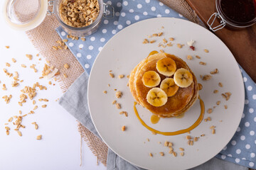 Directly above shot of pancakes with banana slices, honey and oats in plate over napkin on table