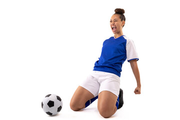 Biracial young female soccer player shouting while kneeling by soccer ball against white background