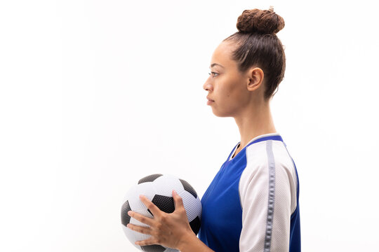 Side view of biracial young female soccer player with soccer ball standing against white background