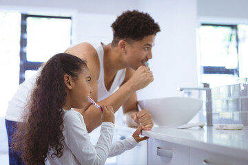 Biracial daughter and father brushing teeth together in bathroom at home